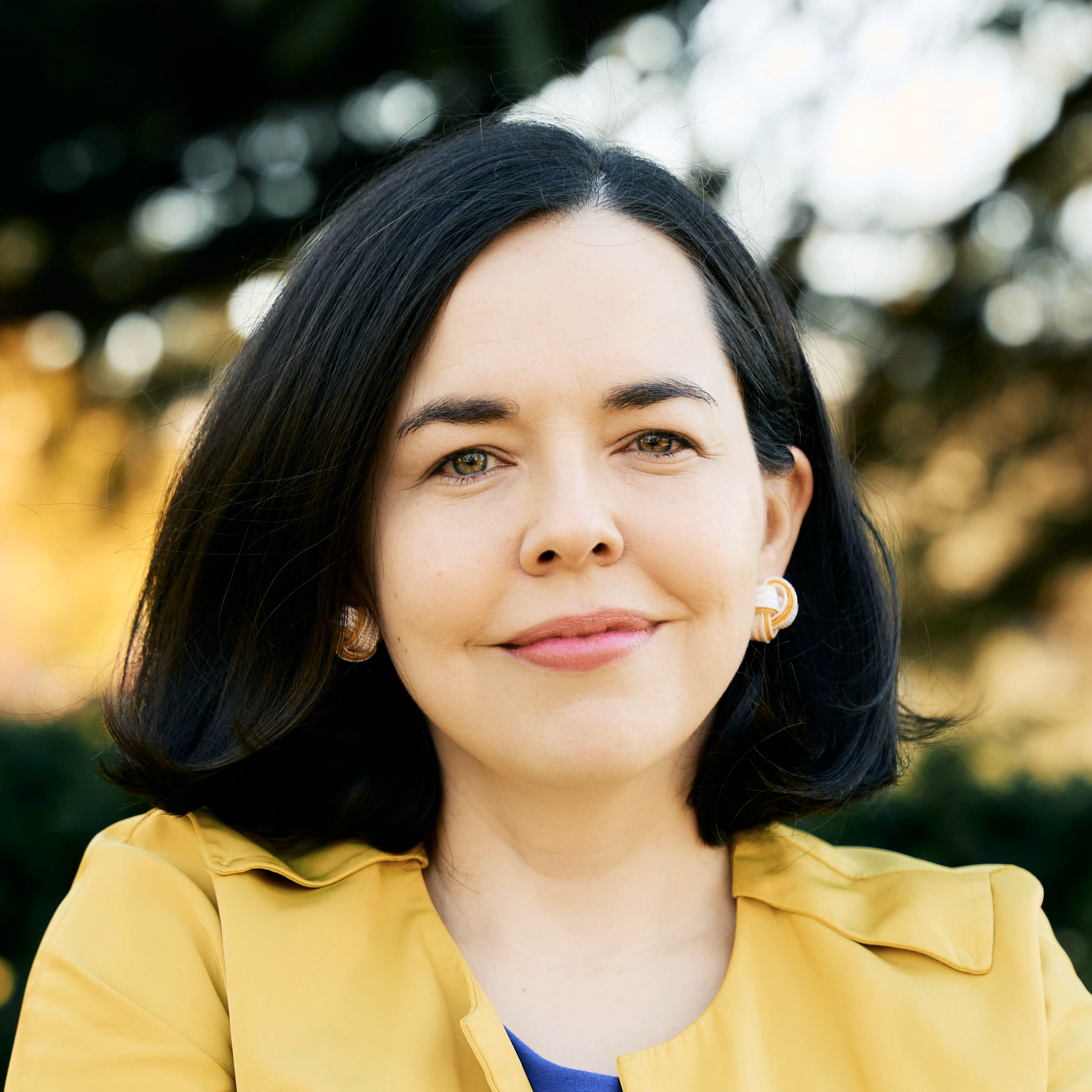 A photo of Tori Liu, woman with black hair wearing a bright yellow jacket, smiling and standing against a neutral background.